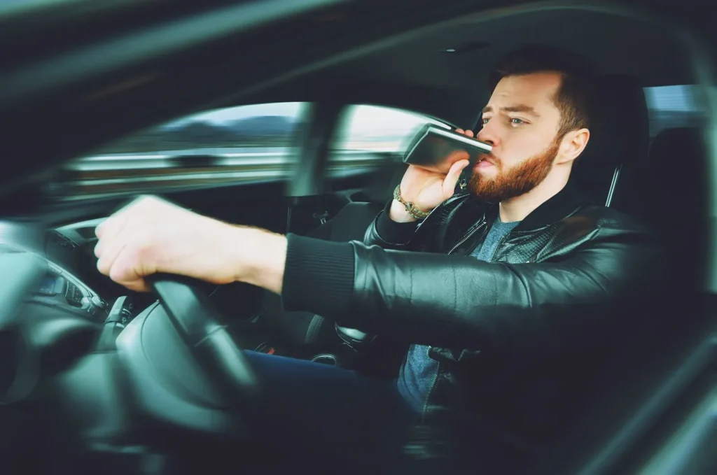 A drunk man drinking while he drives.