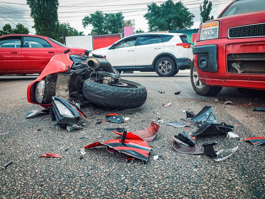 A red motorcycle crashed on the road after hitting a car.